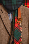 Load image into Gallery viewer, Close-up of a person wearing a tweed jacket with a tartan tie and accessories.

