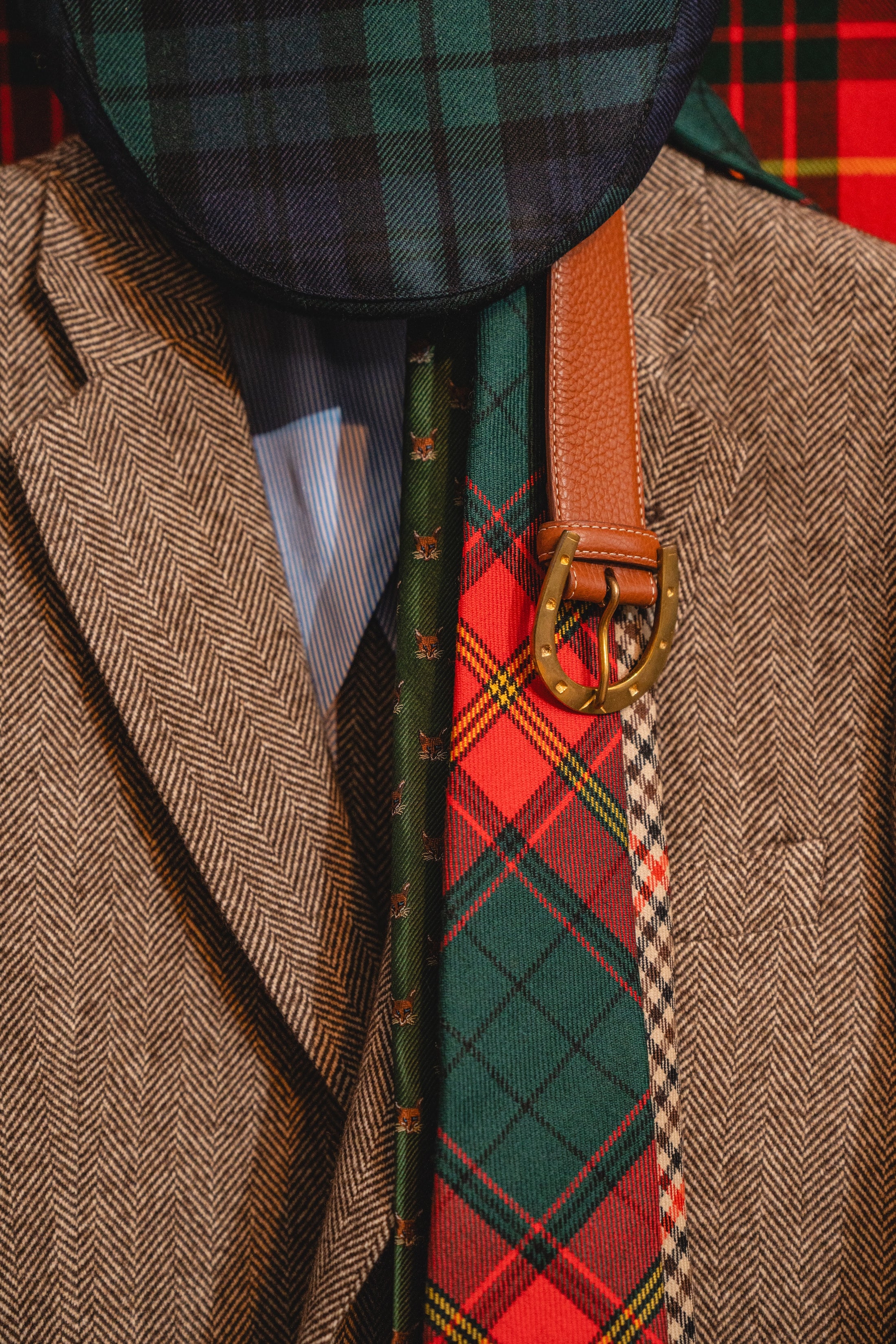 Close-up of a person wearing a tweed jacket with a tartan tie and accessories.