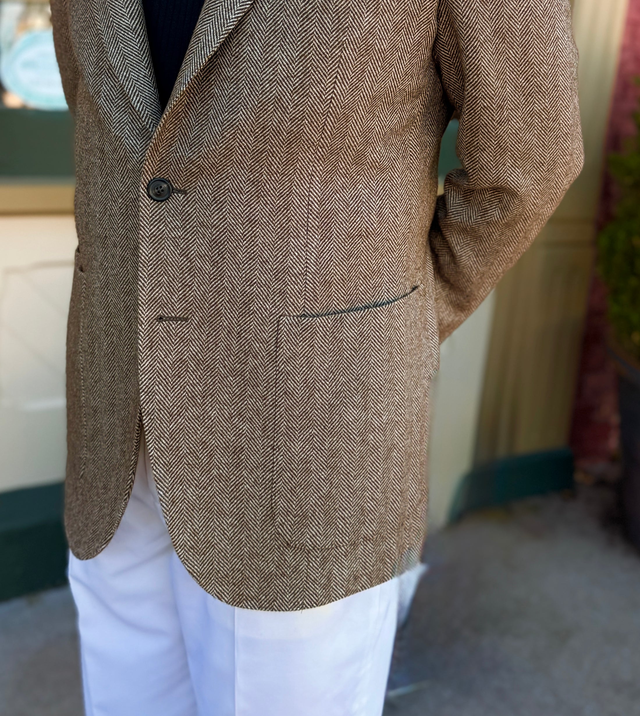 Brown tweed blazer worn with white pants against a neutral background